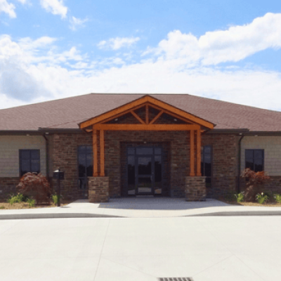 Front view of Aspen Management’s office building with stone veneer, cedar timber entrance, shingle roof, and landscaped surroundings.