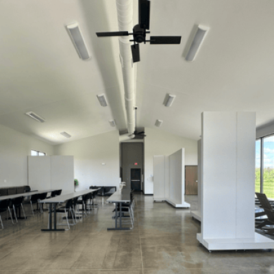 Interior view of the Davy McClure Outdoor Education Center with tall windows, classroom seating, and a children's play area filled with nature-themed elements.
