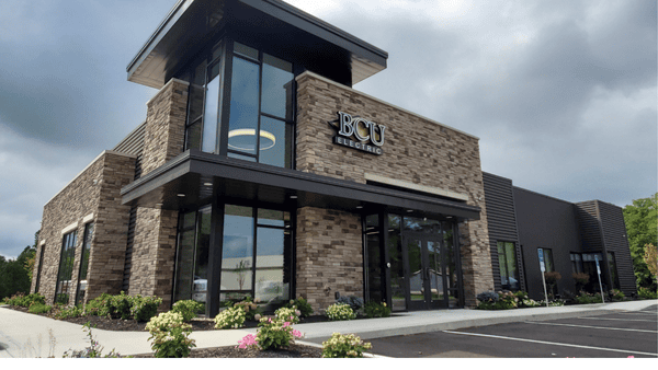 Exterior view of the BCU Electric headquarters, featuring a modern building with stone and metal siding, large glass windows, and a well-maintained landscape under a cloudy sky