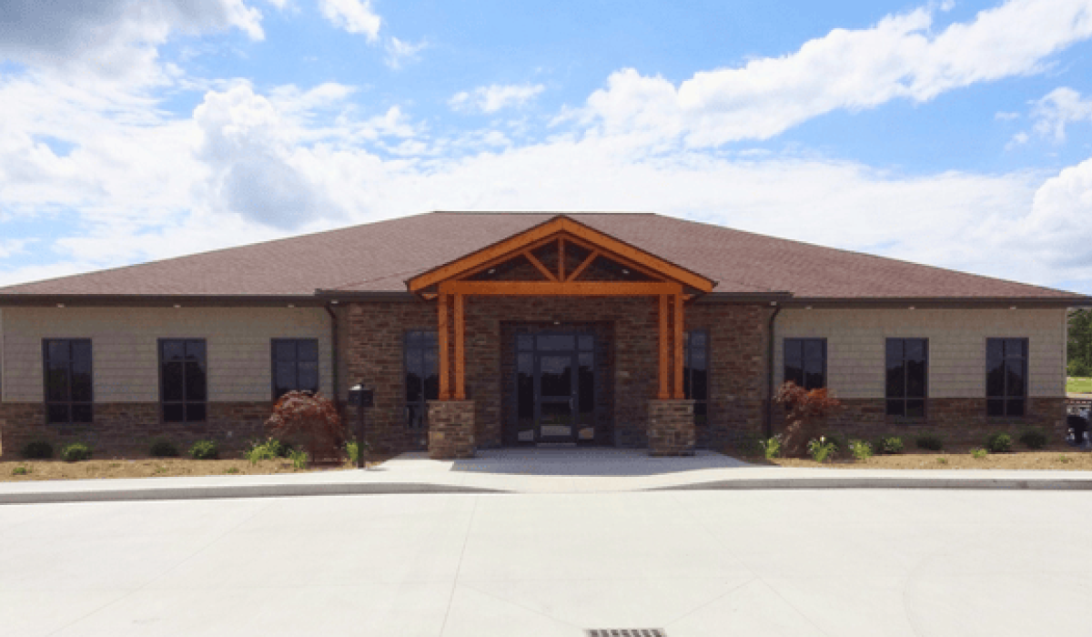 Front view of Aspen Management’s office building with stone veneer, cedar timber entrance, shingle roof, and landscaped surroundings.