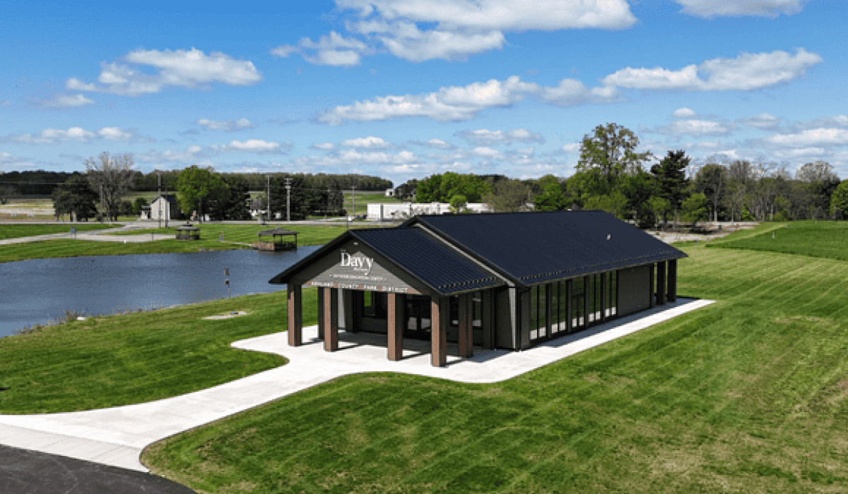 Exterior view of the Davy McClure Outdoor Education Center featuring a vaulted roof, Azek siding, large windows, and a canopy-covered patio surrounded by natural parkland.
