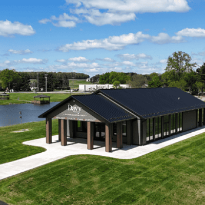 Exterior view of the Davy McClure Outdoor Education Center featuring a vaulted roof, Azek siding, large windows, and a canopy-covered patio surrounded by natural parkland.