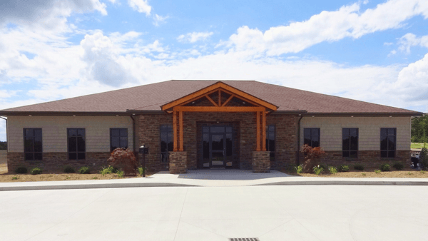 Front view of Aspen Management’s office building with stone veneer, cedar timber entrance, shingle roof, and landscaped surroundings.